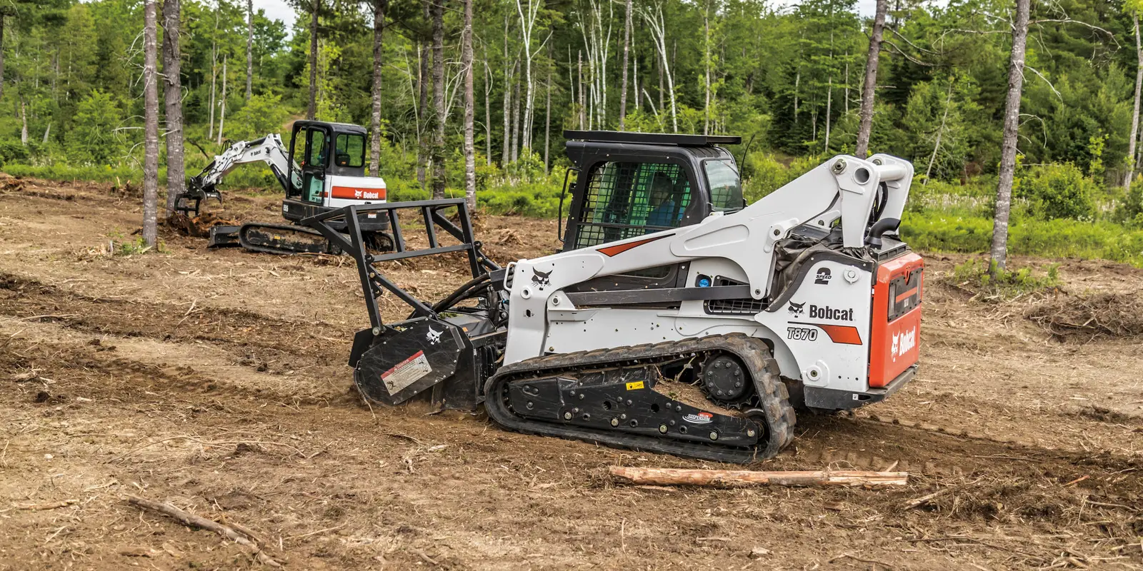 Bobcat compact track loader with a forestry mulcher in front of a white Bobcat excavator on a cleared, mulched site
