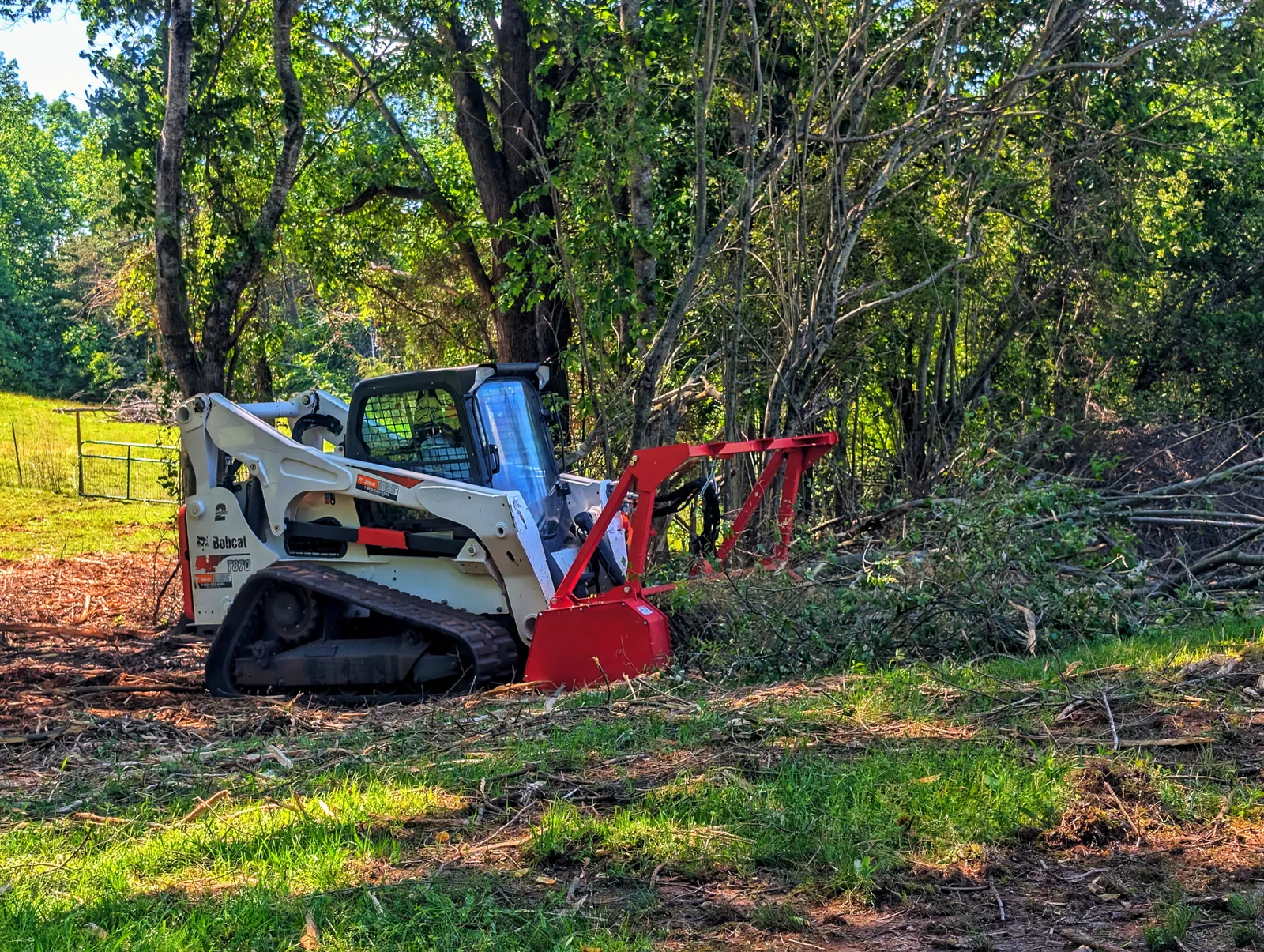 Skid steer working into a wall of thick green brush and undergrowth along a fence line