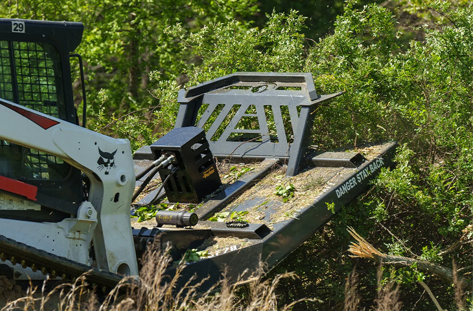 Skid steer running a heavy brush mower deck through tall grass and light brush