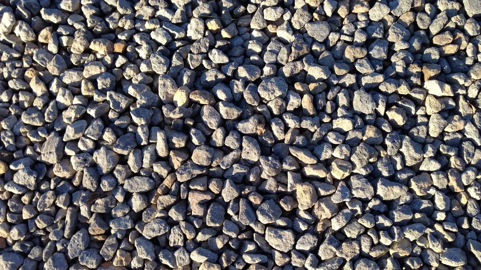 Close view of crushed gravel rock spread across a driveway, the material that sits on top of the grading cost